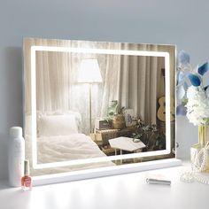 a white table with a lamp and flowers on it next to a mirror that is reflecting a bedroom scene