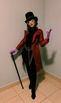 a woman in a red coat and black top hat holding a cane while standing on tiled floor