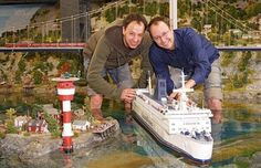 two men standing next to each other in front of a model ship