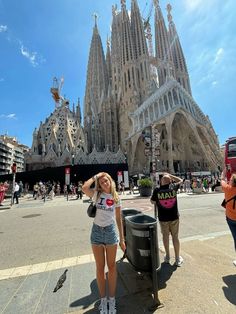 a woman standing next to a trash can in front of a building with spires