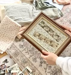 a person holding up a framed photo on top of a floor covered in old clothes