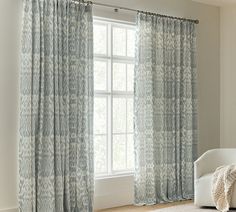 a white chair sitting in front of a window next to a large window with blue curtains