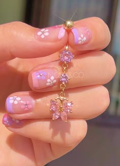 a person with pink and white nail polish holding a gold beaded ring in their hand