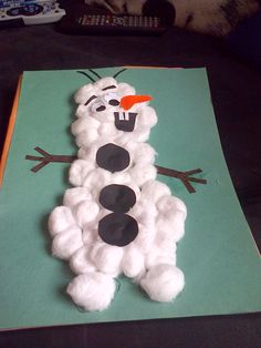 a snowman made out of cotton balls sitting on top of a green sheet of paper