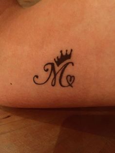 a woman's lower arm with a crown and letter m tattoo on her left side