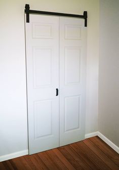 an empty room with two white doors and wood flooring on the side of the wall