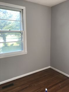 an empty room with a window and hard wood flooring in the corner is painted gray