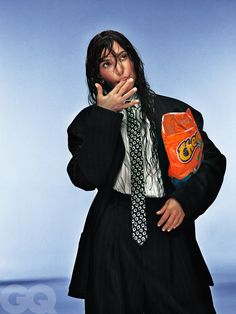 a man in a suit and tie holding an orange object to his mouth while standing against a blue background