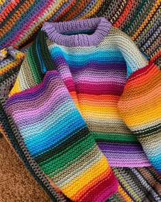 a multicolored crocheted sweater laying on top of a brown carpet next to a pair of scissors