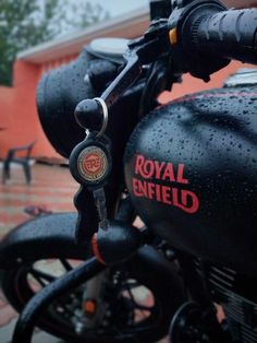 the royal enfield motorcycle is parked in front of an orange building on a rainy day