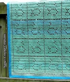 a blue crocheted blanket hanging from a wooden fence