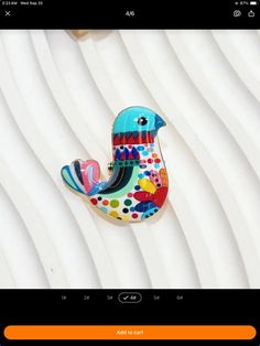 a colorful bird brooch sitting on top of a white table next to a cell phone