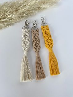 three tasseled keychains on a white surface with an animal's tail in the background