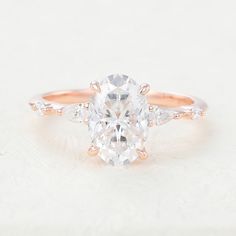 an oval cut diamond ring with three side stones on the band, set in 18k rose gold