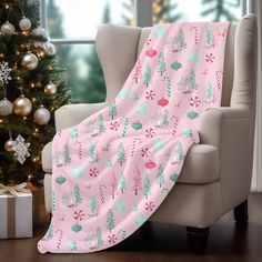 a pink christmas blanket sitting on top of a chair next to a tree and presents