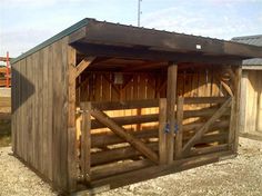 a horse stable with wooden doors and windows on the roof, in front of a barn