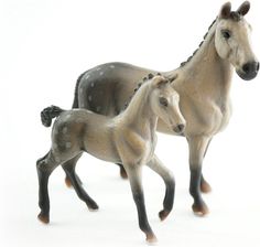 two toy horses standing next to each other on a white surface with one horse looking at the camera