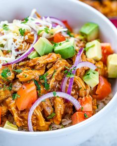 a white bowl filled with rice, meat and veggies next to sliced avocado