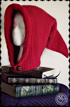 a red knitted hood sitting on top of books