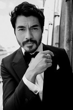 a man in a tuxedo adjusts his bow tie while posing for the camera