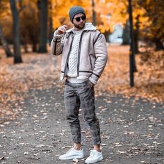 a man standing in the middle of a leaf covered park wearing a hat and jacket