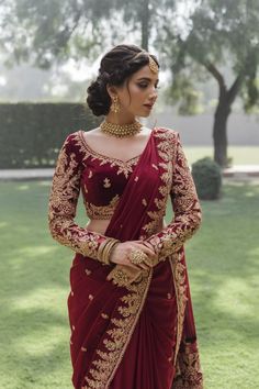 A photo of a Pakistani bride wearing a rich red bridal saree with intricate golden embroidery along the borders. The saree is paired with a matching blouse that has bold golden motifs on the sleeves and neckline. Red Wedding Sarees For Bride, Golden Bridal Saree, Red Saree Bridal Look, Red Bridal Blouse Designs, Bridal Red Saree, Red Bridal Saree, Nepali Bride, Tassels Fashion Clothing