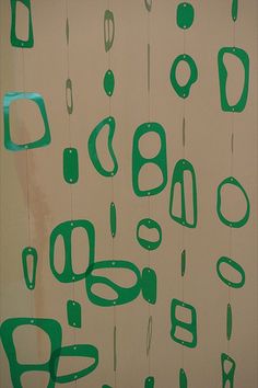 green and white artwork hanging from strings on the side of a wall in front of a window