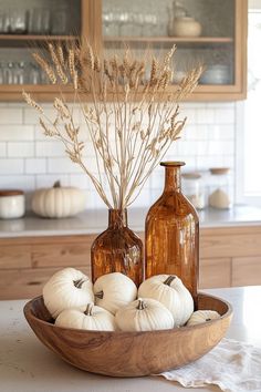 some white pumpkins are sitting in a bowl on the kitchen counter next to two brown bottles