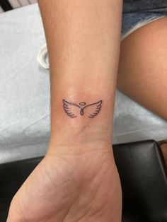 a small tattoo on the wrist of a woman's hand, with an angel wing