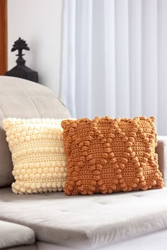 two knitted pillows sitting on top of a white couch