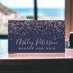 a business card with gold confetti on it sitting on a desk in front of a window