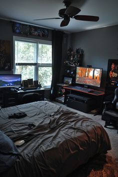 a bedroom with a bed, desk and two computer monitors on the wall in front of a window