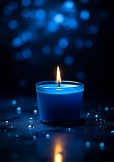 a blue candle is lit on a dark surface with water droplets around it and the light shining brightly