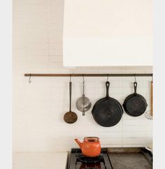 pots and pans are hanging on the wall above an oven with two burners