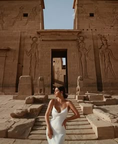 a woman in a white dress standing next to an egyptian temple with statues on it