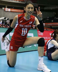 a woman in red uniform standing on top of a blue court with her hand up