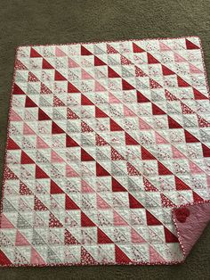 a red and white quilt on the floor next to a pink rug with a heart