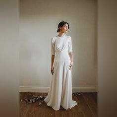 a woman standing in front of a wall wearing a white dress