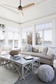 a living room filled with white furniture and lots of windows next to a body of water