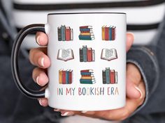 a person holding a coffee mug with books on it that says in my bookish era