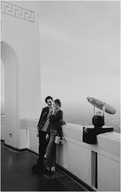 black and white photograph of two people standing next to each other on top of a building