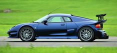 a blue sports car driving down a road next to a green grass covered field in the background