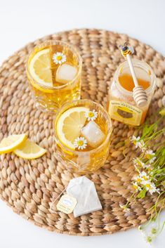 three glasses filled with lemonade sitting on top of a woven place mat next to flowers