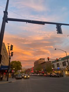 the sun is setting over an intersection with cars and buildings on either side of it