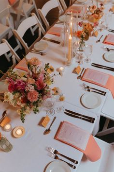 a long table set with place settings and flowers on it for a formal dinner or party