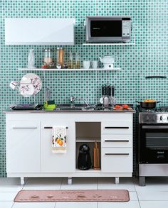 a kitchen with white cabinets and green tiles on the wall, along with a black stove top oven