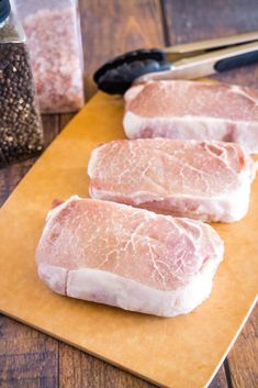 three raw pork chops sitting on top of a cutting board next to seasoning