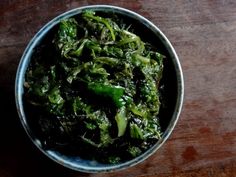 a bowl filled with green vegetables on top of a wooden table