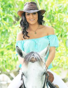 a woman wearing a hat riding on the back of a white horse in front of trees