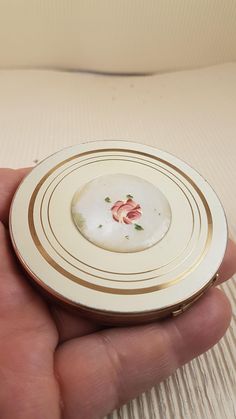 a hand holding a white and gold plate with red flowers on the inside of it